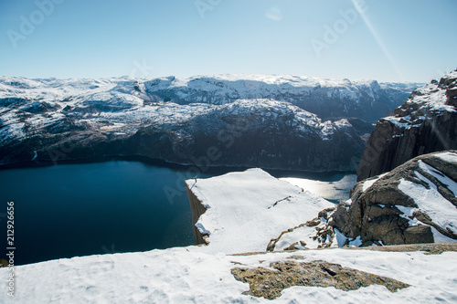 Happy man raised hands while standing near the precipice with scenic view of the water channel with mountains. Preikestolen, Lysefjord, Norway. Taveling concept. Top view. photo