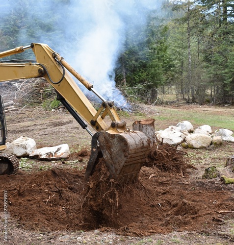 Excavator bucket picking up dirt and tree roots