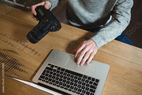 Man using laptop while holding digital camera photo