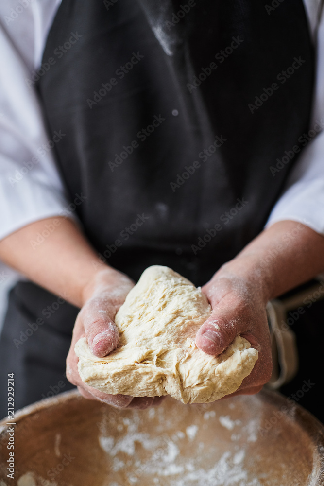 Slow motion shot of baker hands kneading dough in flour in wooden bowl