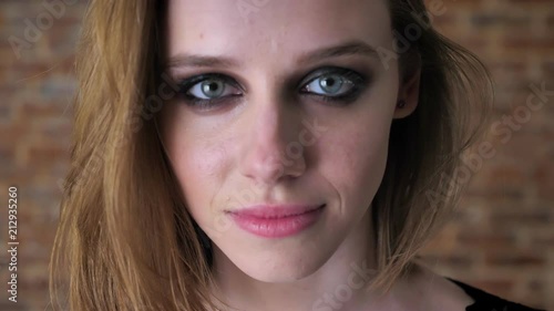 Face of young charming girl with smoky eyes is watching at camera, blurred background