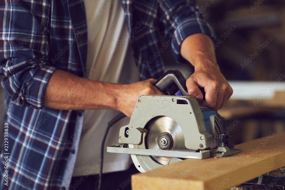 Close-up of carpenter using circular saw for cutting a wooden plank