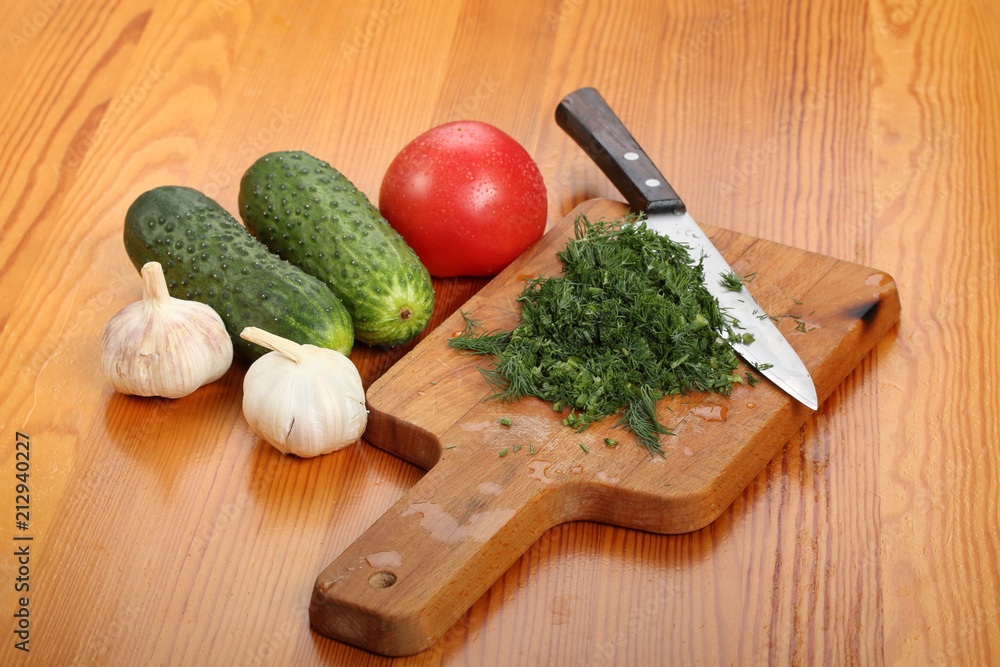 Сutting board with chopped dill leaves and knife on a wooden table
