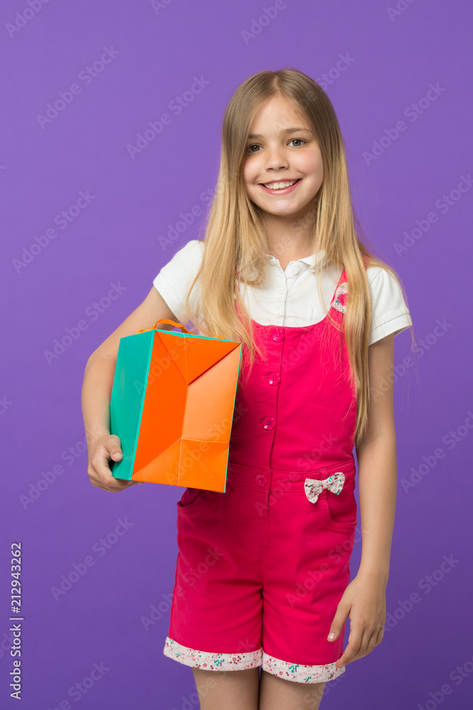 Happy girl with shopping bag on violet background. Little shopaholic smile with paper bag. Child shopper smiling with purchase. Holidays preparation and celebration. Shopping and sale Happy girl with shopping bag on violet background. Little shopaholic smile with paper bag. Child shopper smiling with purchase. Holidays preparation and celebration. Shopping and sale