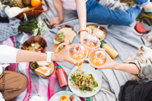 Tableau sur toile Close up girls holding cup to go with orange juice on beautiful picnic with vari