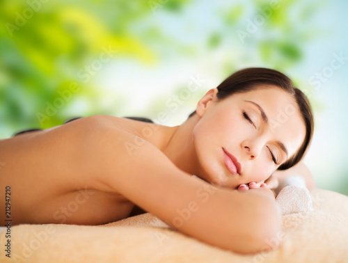 wellness, spa and beauty concept - beautiful woman having hot stone therapy over green natural background