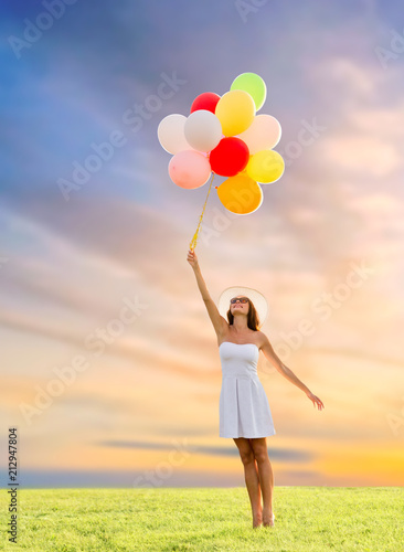 happiness, summer and people concept - smiling young woman wearing sunglasses with balloons on meadow over sunset sky background