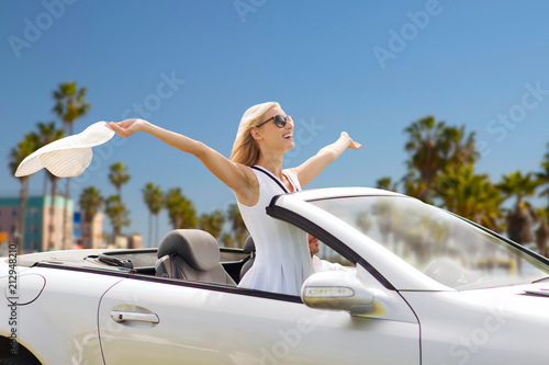 road trip, travel and people concept - happy couple driving in convertible car over venice beach background in california