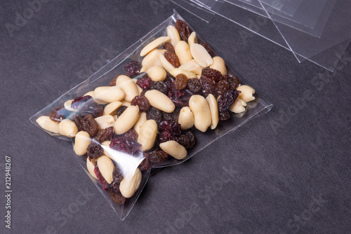 Billede på lærred nuts and raisins in cellophane bag on black background