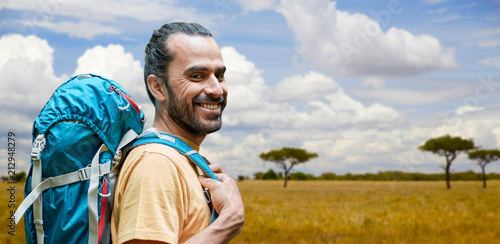 adventure, travel, tourism, hike and people concept - smiling man with backpack over african savannah background
