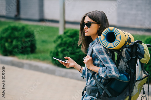 young female backpacker in sunglasses holding smartphone