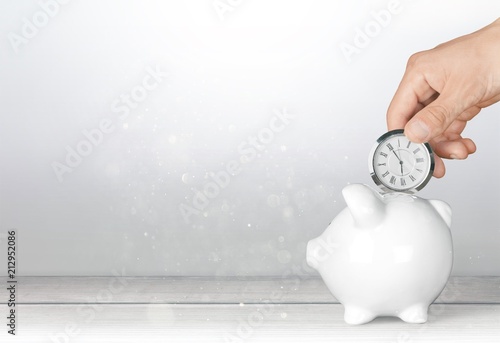 Hand depositing clock in piggy bank