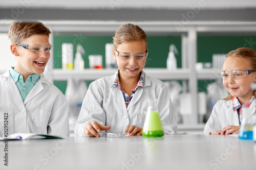 education, science, chemistry and children concept - kids or students with test tube making experiment at school laboratory