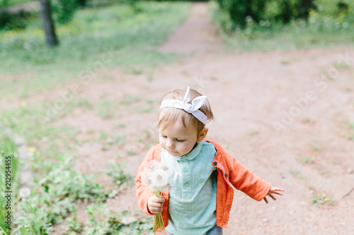 Portrait of adorable baby girl holding white dandelion in summer park