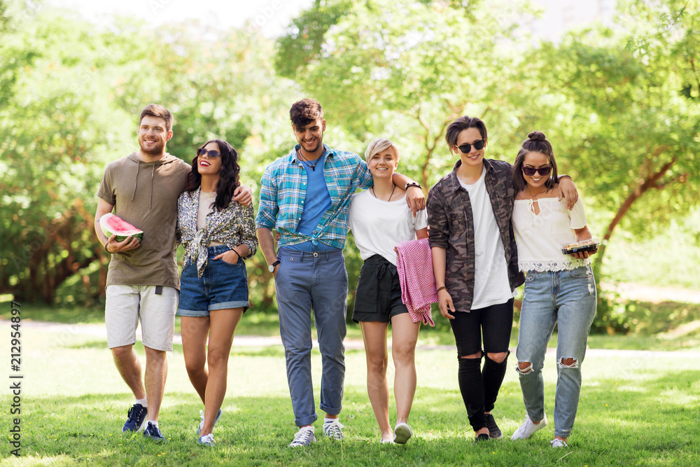 friendship and leisure concept - group of happy friends with picnic blanket and watermelon walking at summer park friendship and leisure concept - group of happy friends with picnic blanket and watermelon walking at summer park