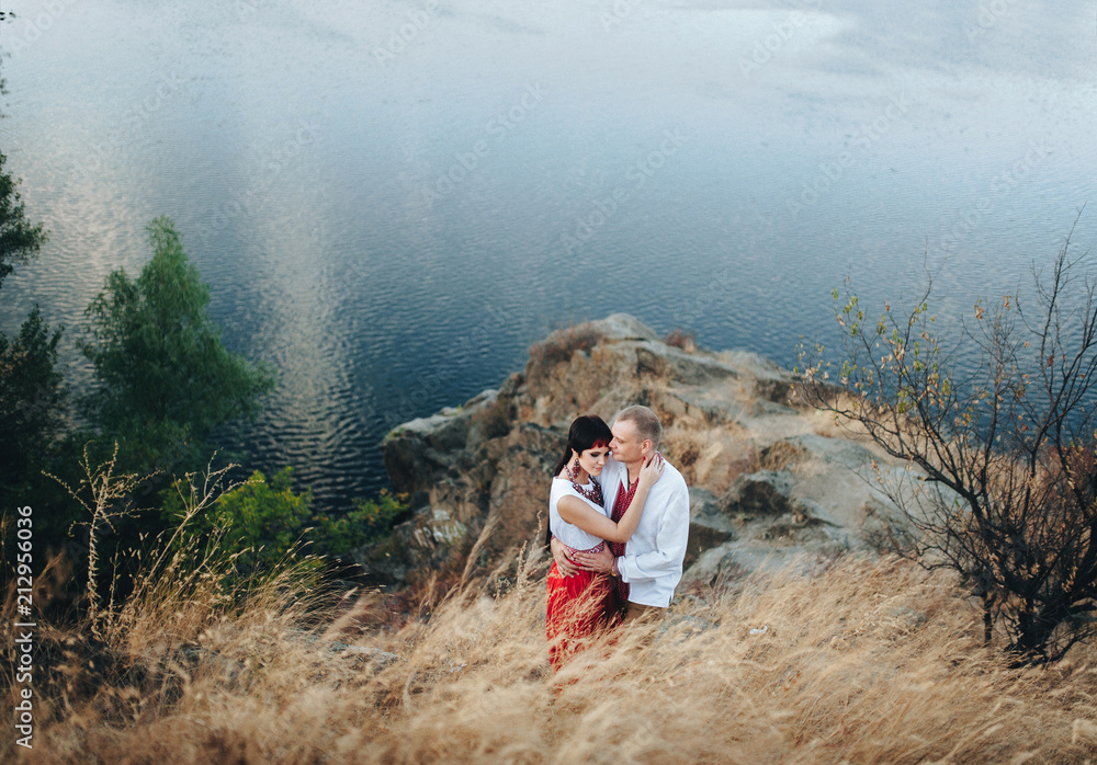 A couple in Ukrainian national clothes romantic embrace near the river. Ukrainian wedding in ethnic traditions. Khortytsya, top view, copy space.
