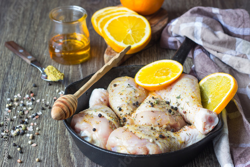 Raw food. Chicken legs (drumsticks) with orange and mustard marinade in cast-iron pan on wooden table background. Cooking content