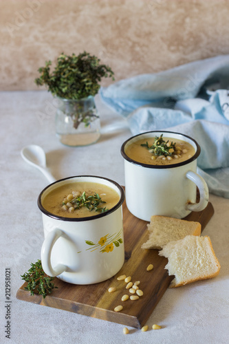 Soup, orange cream of pumpkin, carrot and lentil soup in mug served with pine nuts and thyme. Winter and autumn vegetarian food concept. 