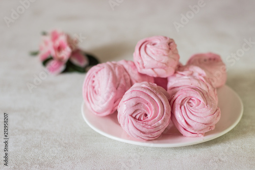 Beautiful delicious dessert. Pink zephyr on a white plate and pink flower. Berry zephyr on light gray background. 