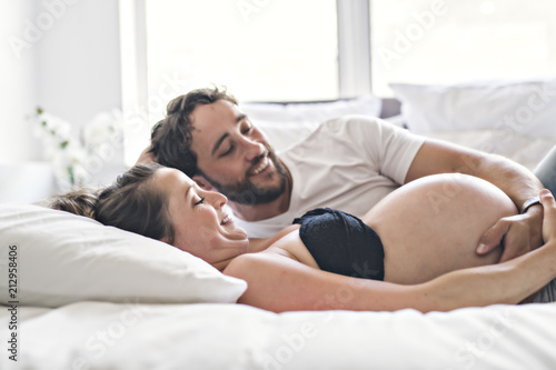 Man with pregnant woman in bed at home having great time