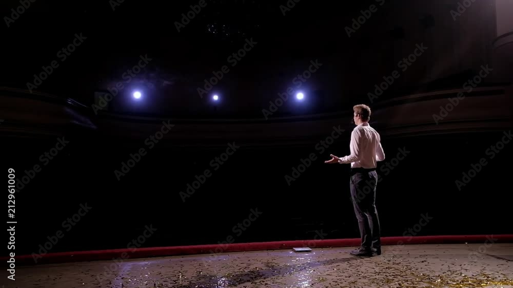 Back view of businessman speaker standing on podium in lights, Person says about marketing and management for successful sales to college students indoors closeup. Back view of businessman speaker standing on podium in lights, Person says about marketing and management for successful sales to college students indoors closeup.