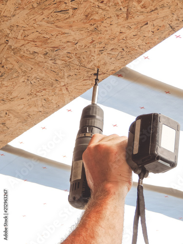 Builder twists the screw in the OSB sheet on the ceiling