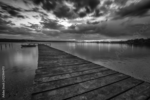Black and white landscape with wooden pier and fishing boat at the lake after sunset