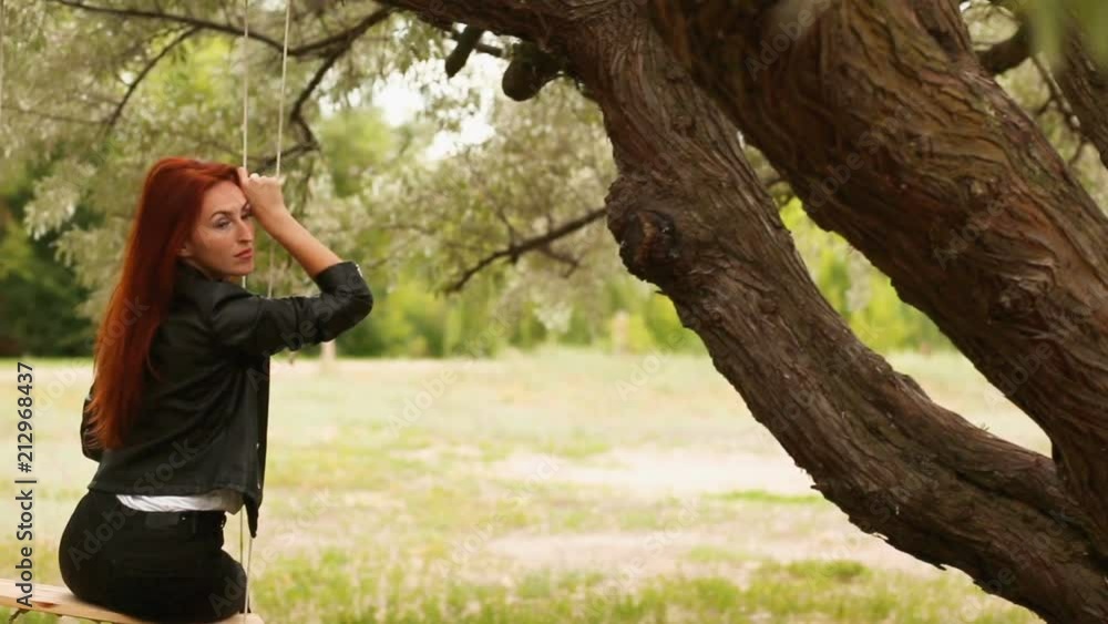 Young woman is swinging on a swing in spring forest. looks away and smiles