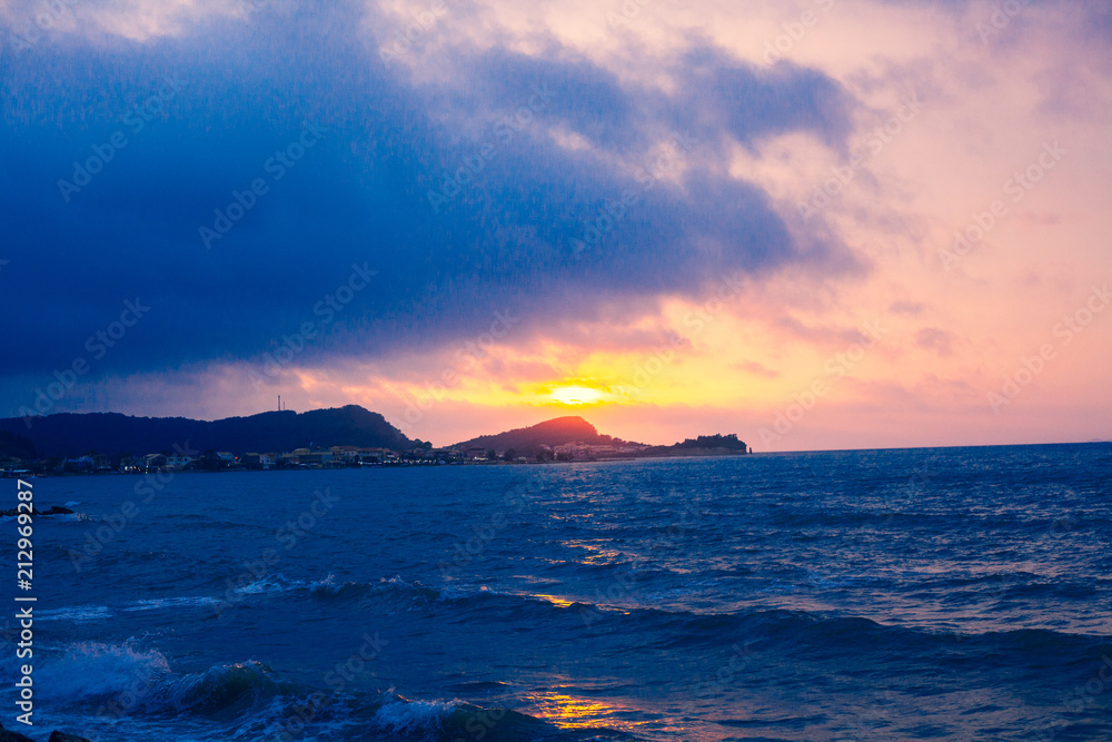 Sunset Sea Perspective from the Shoreline, Beautiful Mountain and Ocean view Landscape, Shimmering Twilight with blue and dark colors, Hidding Sun between Cloudy Sky