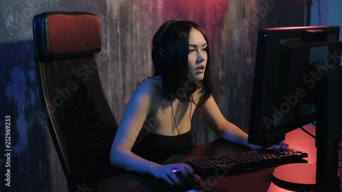 Happy cheerful cute sexy gamer girl sitting at home playing video games alone on a pc computer, then hand gesture of win and pure emotion. photo