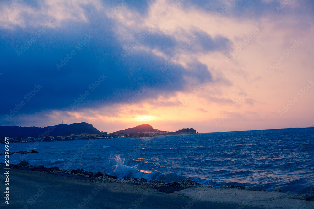 Sunset Sea Perspective from the Shoreline, Beautiful Mountain and Ocean view Landscape, Shimmering Twilight with blue and dark colors, Hidding Sun between Cloudy Sky