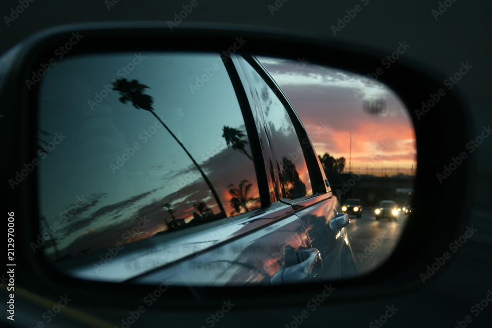 Sunset in Los Angeles seen from the side mirror of a car driving along the road