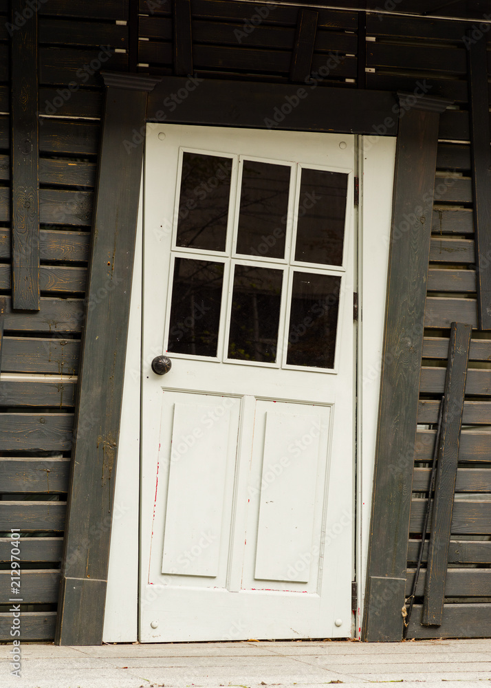 Fototapeta premium White entrance wooden door with visual tilt effect in a black wooden wall