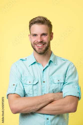 Cheerful consultant. Man smiling face posing confidently with folded arms yellow background. Man shop consultant looks cheerful confident and hospitable. Guy with bristle glad to help you in shop © be free