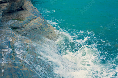 Bright Blue Ocean Surface with Waves and Foaming crashing againts the natural clay wall, Dark Turquoise Water Waving at the pace of the Breeze, Mediterranean Sea Landscape View from the Sky,