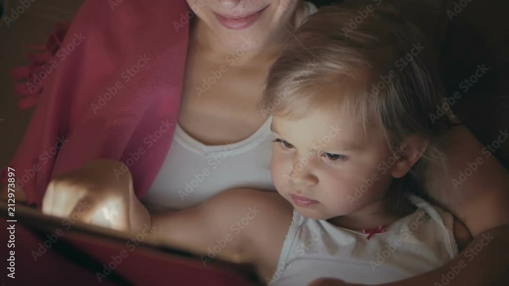 Mom with a little daughter lying on the bed watching the screen of the electronic tablet Mom with a little daughter lying on the bed watching the screen of the electronic tablet