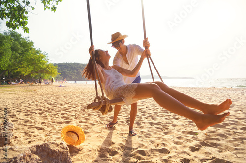 Romantic couple in love playing together on rope swing at summer beach for fun and happy smile. young man and woman on holidays or honeymoon