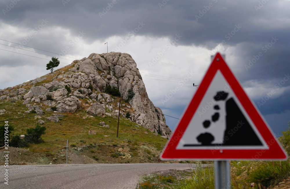 Falling rocks of landslide road sign and rocky hill in background, selective focus