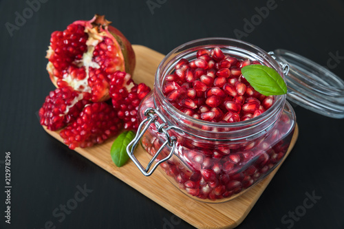 Delicious pomegranate seeds placed in glass jar with fresh organic pomegranates on rustic wooden background.Close up,Copy space