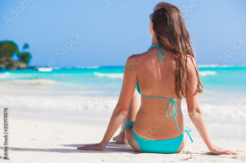 young longhaired woman in sunglasses and bikini smiling and sunbathing by the beach photo