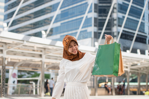 Beautiful malaysia young woman a smiling and happy with shopping bags, lifestyle concept in the big city, the business district with skyscrapers in the Background