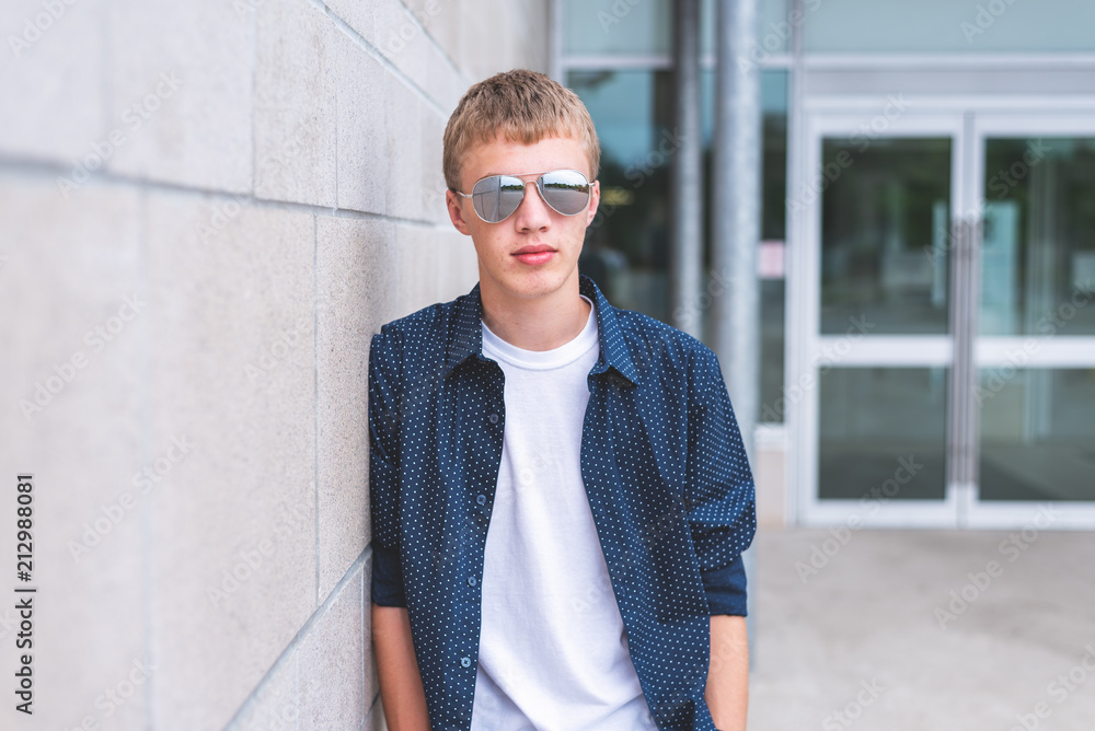 Serious teen wearing sunglasses and leaning against a brick wall. Serious teen wearing sunglasses and leaning against a brick wall.