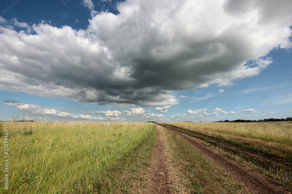 summer landscape with clouds over the road in the field