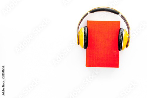 Audiobooks concept. Headphones put over hardback book with empty cover on white background top view copy space