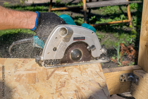 a man sawing a Board with a power tool, chips fly in all directions. Construction, wood processing