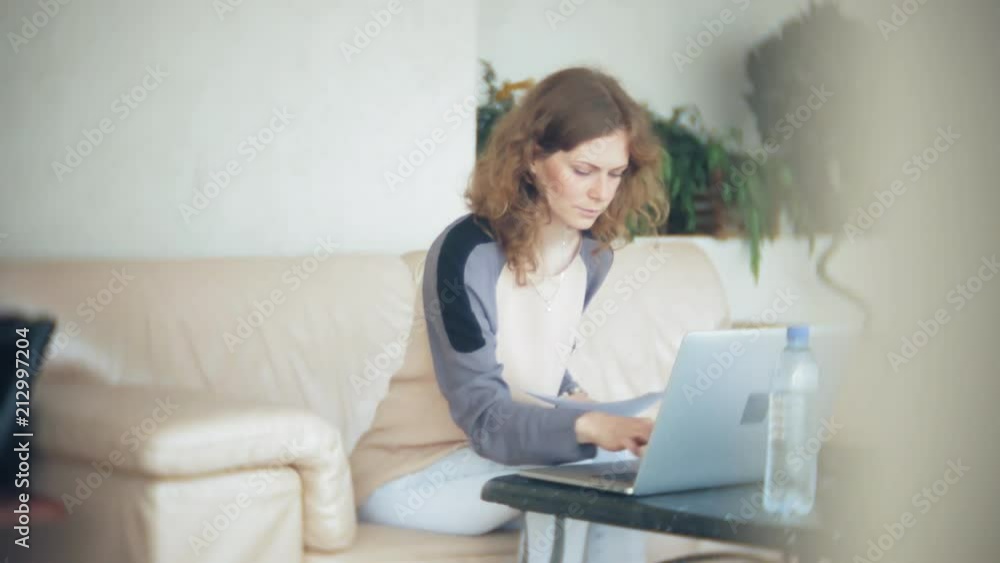 Young beautiful business woman sitting on sofa at table with tablet and looking through paper Young beautiful business woman sitting on sofa at table with tablet and looking through paper