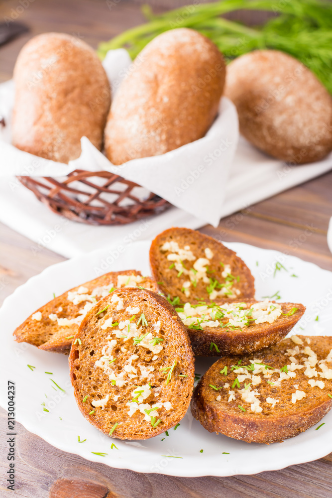 Fresh rye garlic croutons with dill on a plate and buns in a basket on a wooden table Fresh rye garlic croutons with dill on a plate and buns in a basket on a wooden table