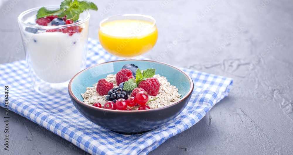 Delicious and healthy breakfast, gray background and napkin. Yogurt, muesli, granola, raspberry and blueberry berries and fresh orange juice. Copy space, Delicious and healthy breakfast, gray background and napkin. Yogurt, muesli, granola, raspberry and blueberry berries and fresh orange juice. Copy space,