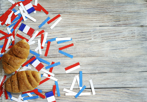 Paper confetti of national colors of France, white-blue-red on a white wooden background with flags and croissants, concept Bastille day, July 14 in France