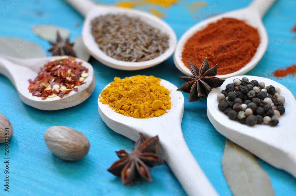Concept of table with colorful spices in wooden spoons on blue background, close up, selective focus